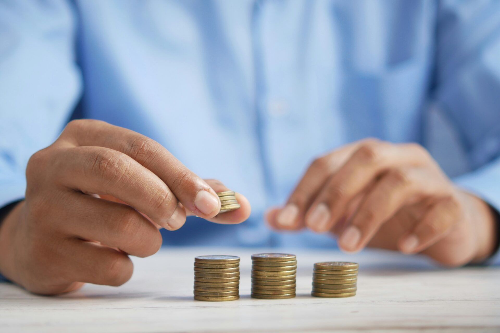 Man in blue shirt stacking coins, inferring wealth.